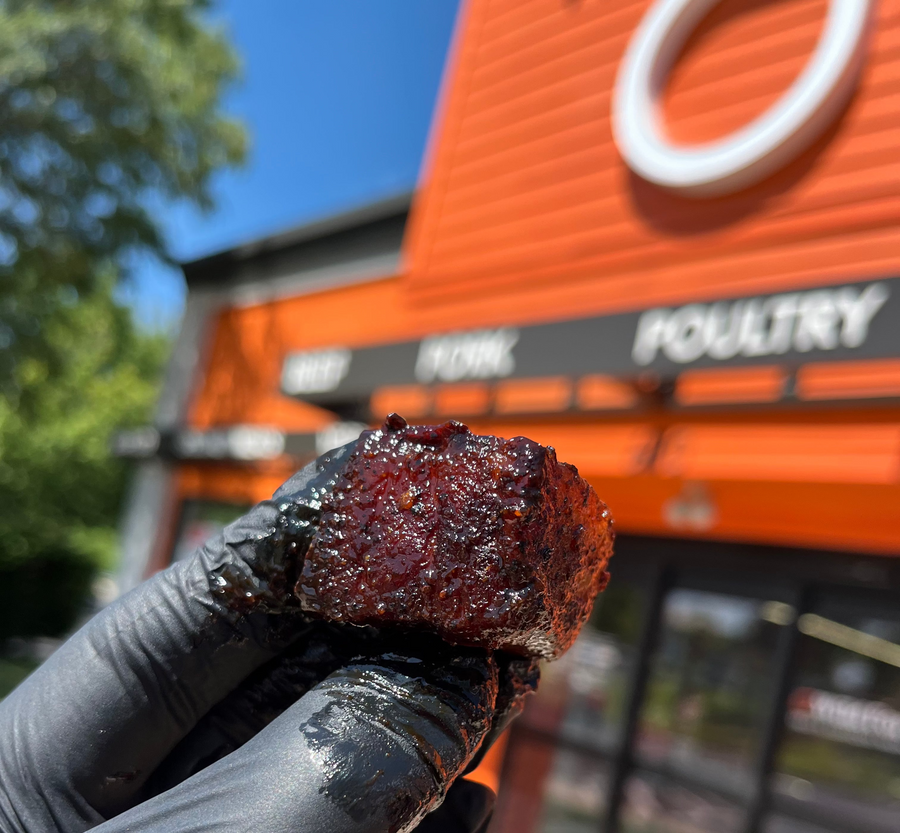 Chris Apple holding up a perfectly cooked pork belly burnt ends infront of a Wild Fork Foods location that White Bulls BBQ was hosting a pop-up event at. 